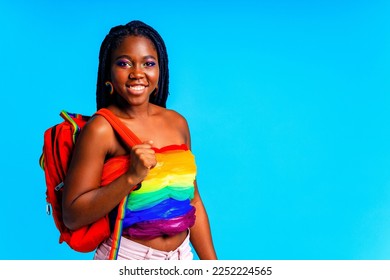 young woman wearing colorful blouse holding backpack isolated over blue background, lgbt concept