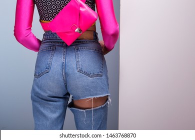 Young Woman Wearing Colorful Long Sleeve Top And Magenta Fanny Pack Belt Bag, 80s Fashion Look With High Waist Ripped Jeans, Back View