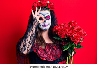 Young Woman Wearing Day Of The Dead Costume Holding Flowers Smiling Happy Doing Ok Sign With Hand On Eye Looking Through Fingers 