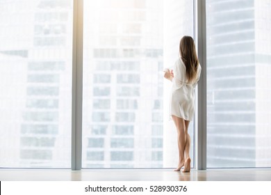 Young Woman, Wearing Dress Gown Looking Through Floor Window, Waiting For A Busy Husband, Dreaming Of A Job In Big City, First Day In Unknown Town, Ready To Conquer The Capital. Rear View, Full Length