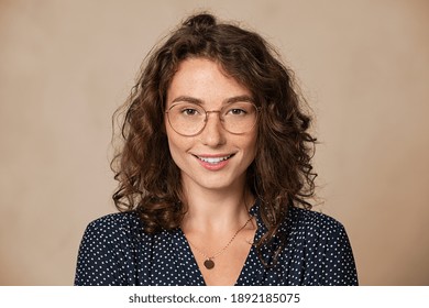 Young woman wearing eyeglasses isolated on beige background and looking at camera. Proud female student with nerd glasses isolated on wall. Sophisticated glamour girl in shirt wearing big spectacles.