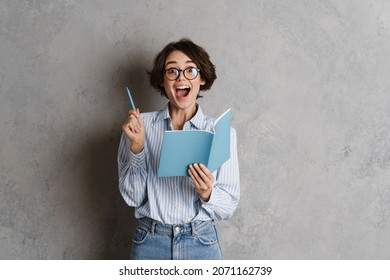 Young woman wearing eyeglasses writing down notes in planner isolated over grey wall - Shutterstock ID 2071162739