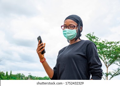 A Young Woman Wearing A Face Mask Holding Up Her Mobile Phone