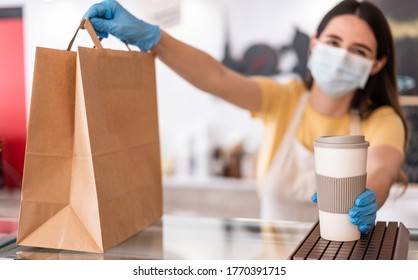 Young Woman Wearing Face Mask While Serving Takeaway Breakfast And Coffee Inside Cafeteria Restaurant - Worker Preparing Delivery Food Inside Bakery Bar During Coronavirus Period - Focus On Right Hand