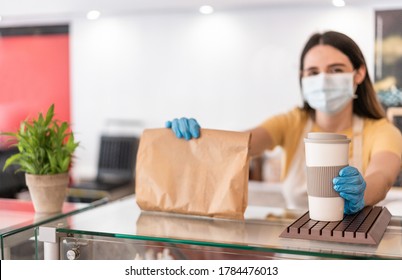 Young Woman Wearing Face Mask While Serving Takeaway Breakfast And Coffee Inside Cafeteria Restaurant - Worker Preparing Delivery Food Inside Bakery Bar During Coronavirus Period - Focus On Right Hand