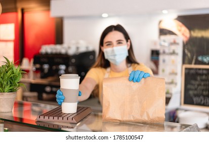 Young Woman Wearing Face Mask While Serving Takeaway Breakfast And Coffee Inside Cafeteria Restaurant - Worker Preparing Healthy Food Inside Cafè Bar During Coronavirus Period - Focus On Left Hand