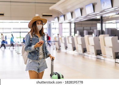 Young Woman Wearing A Face Mask And Holding A Mobile Phone Is Looking For A Check-in Counter At The Airport, New Normal Lifestyle Concept