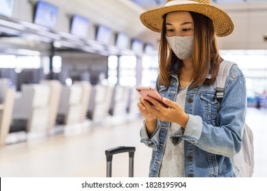 Young Woman Wearing A Face Mask And Using A Mobile Phone Is Looking For A Check-in Counter At The Airport, New Normal Lifestyle Concept