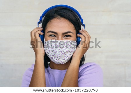 Young woman wearing face mask listening to music with wireless headphones - Latin girl using protective facemask for preventing spread of corona virus - Outbreak health care and technology concept 