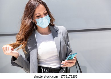 Young woman wearing formal clothes listening to music through her smartphone on the street. She is wearing a medical mask as a preventive measure for the Covid-19 health crisis. New normal concept. - Powered by Shutterstock