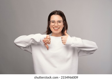 Young Woman Wearing Glasses Is Showing Thumb Up And Down With Both Hands.