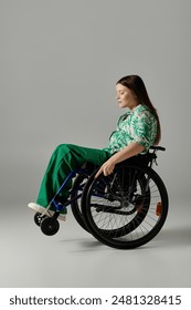 A young woman wearing green attire sits in a wheelchair against a gray background, her eyes closed in a moment of peaceful reflection.