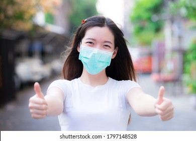 Young Woman Wearing Green Medical Face Mask. Person Showing Thumbs Up And Sweet Smile Under Protection Mask. Protection Coronavirus Disease (Covid-19) And PM 2.5  Concept. 