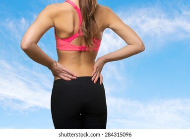 Young woman wearing a gym clothes. She has a back ache. Over clouds background
