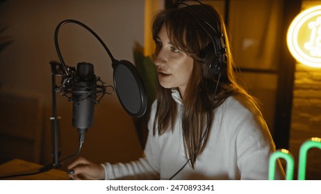 A young woman wearing headphones speaks into a microphone in an intimate radio studio setting, suggesting a live broadcast or podcast recording scenario. - Powered by Shutterstock