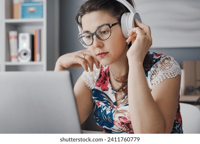 Young woman wearing headphones and watching online videos on her laptop