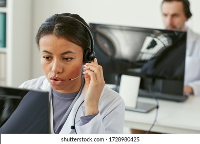 Young woman wearing headphones working on computer she answering on phone calls in medical call centre