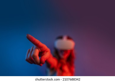 Young Woman Wearing Headset For Augmented Reality. Finger Pointing During VR Experience. Studio Portrait With Color Gels. Focus On Finger, Shallow Depth Of Field.