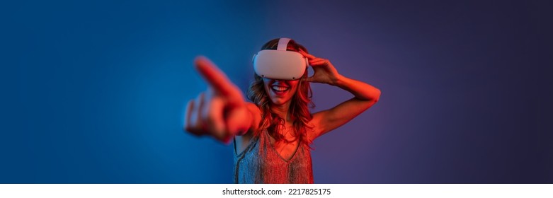 Young Woman Wearing Headset For Augmented Reality. Finger Pointing During VR Experience. Studio Portrait With Color Gels. Focus On Finger, Shallow Depth Of Field.