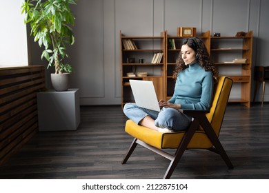 Young woman wearing headset studying online while sitting with laptop in comfortable chair, enjoying distance learning on computer. Remote contact center agent providing customer service from home - Shutterstock ID 2122875104