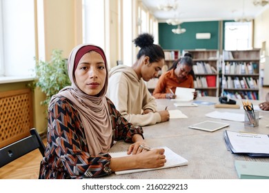 Young woman wearing hijab sitting at table with her classmates looking at camera during English language lesson - Shutterstock ID 2160229213