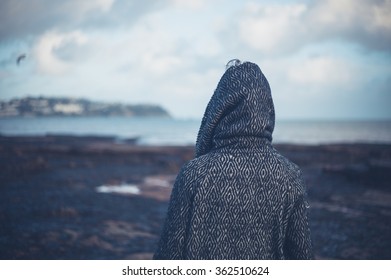 A young woman wearing a hooded coat is walking on a dramatic beach in the winter