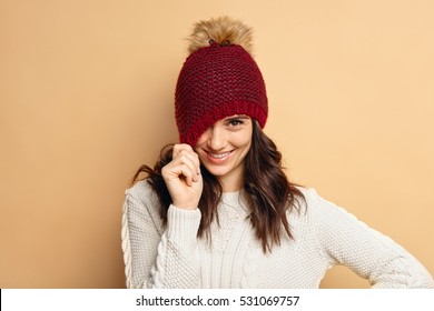 young woman wearing knitted pullover over beige background. Happy smiling girl in winter hat