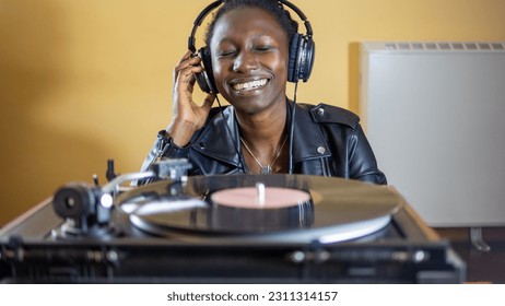 young woman wearing a leather jacket using headphones while playing a vinyl record on a vintage turntable - Shutterstock ID 2311314157