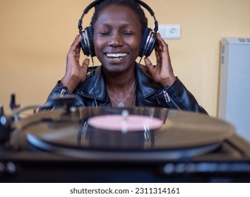 young woman wearing a leather jacket using headphones while playing a vinyl record on a vintage turntable - Shutterstock ID 2311314161