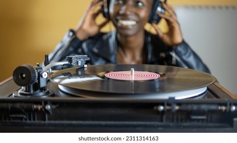 young woman wearing a leather jacket using headphones while playing a vinyl record on a vintage turntable - Shutterstock ID 2311314163