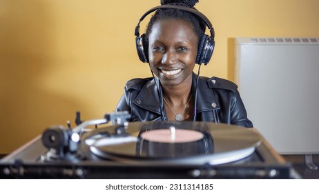 young woman wearing a leather jacket using headphones while playing a vinyl record on a vintage turntable - Shutterstock ID 2311314185