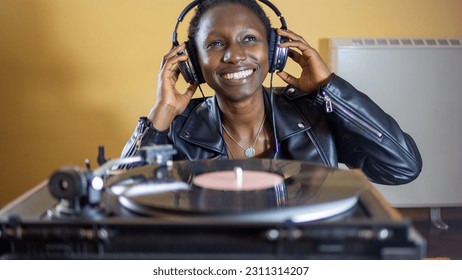 young woman wearing a leather jacket using headphones while playing a vinyl record on a vintage turntable - Shutterstock ID 2311314207