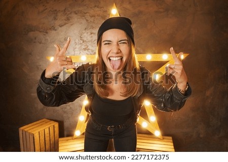 Young woman wearing leather jacket grunge star background shouting with crazy expression doing rock symbol with hands up. Music star. Heavy concept.
