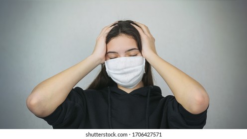 Young Woman Wearing Medical Facemask Holds Head In Hands Health Care Concept Wall Background