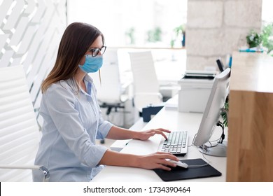 Young woman wearing medical mask in office. Protection employees on workplace. Girl working at reception indoors. Social distancing in public place, disease prevention during quarantine, staff safety. - Shutterstock ID 1734390464
