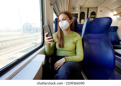 Young Woman Wearing Medical Mask Relaxing In Train Seat While Using Smartphone App. Business Woman Enjoying View Texting On Mobile Phone. Travel Safety Lifestyle.