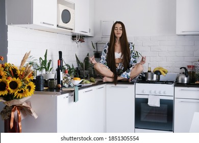Young Woman Wearing Morning Gown And White Underwear Sitting On The Desk In Lotus Pose, Meditating And Concentrating In Morning Kitchen Chaos
