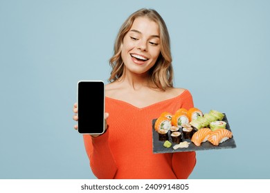 Young woman wearing orange casual clothes hold using blank screen mobile cell phone order online raw fresh sushi roll served on black plate eat Japanese food isolated on plain blue background studio - Powered by Shutterstock