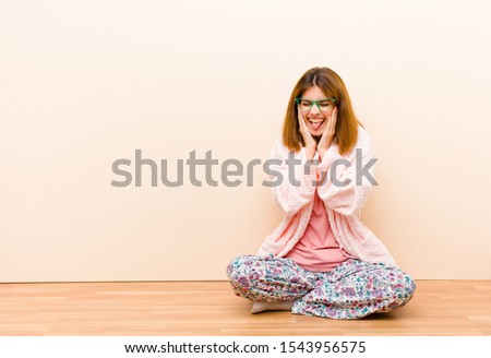 young woman wearing pajamas sitting at home looking goofy and funny with a silly cross-eyed expression, joking and fooling around