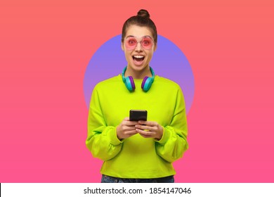 Young woman wearing pink eyeglasses  green neon sweatshirt   headphones around neck  excited by content phone screen