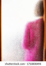 Young Woman Wearing Pink Sweater Behind Closed Door Seen Through Glass. Abstract Portrait.