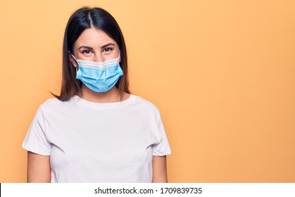 Young Woman Wearing Protection Mask For Coronavirus Disease Over Yellow Background With A Happy And Cool Smile On Face. Lucky Person.