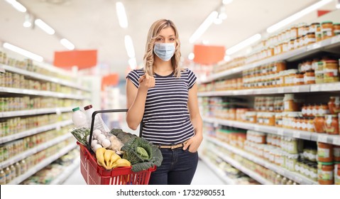 Young Woman Wearing A Protective Face Mask And Carrying A Shopping Basket In A Supermarket