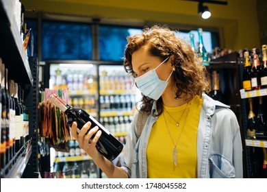 Young woman wearing protective face mask chooses wine in grocery store.