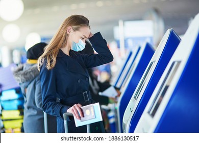 Young woman wearing protective face mask in international airport doing self check-in, stressed and concerned. Missed, delayed or canceled flight concept. Traveling during pandemic