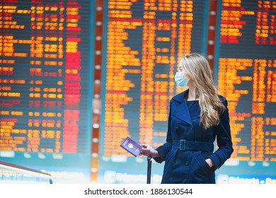 Young Woman Wearing Protective Face Mask In International Airport Near The Flight Information Board, Checking Her Passport. Traveling During Pandemic