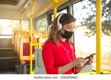 A Young Woman Wearing A Protective Mask And White Headphones Listening To Music On A Public Bus.