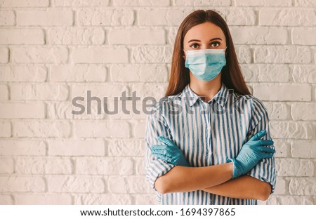 Young woman wearing protective mask on face and medical gloves keeping arms crossed in hospital. Confident girl, female doctor in medical mask and protective gloves. Coronavirus COVID-19 protection