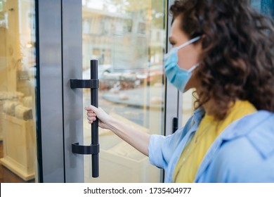 Young Woman Wearing Protective Medical Mask Holds On To The Handle And Opens The Door When Entering Store.