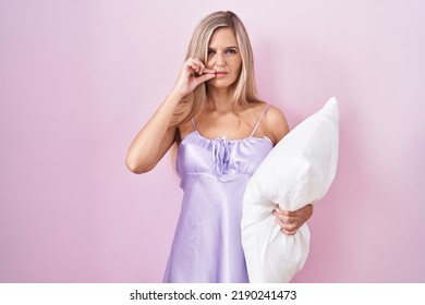 Young Woman Wearing Pyjama Hugging Pillow Mouth And Lips Shut As Zip With Fingers. Secret And Silent, Taboo Talking 